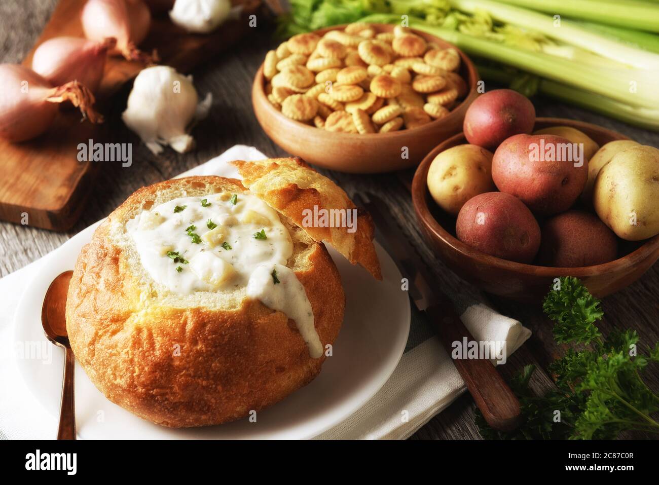 New England Clam Chowder Still Life: Una ciotola di pane piena di zuppa fresca fatta in casa con cracker e ingredienti. Foto Stock