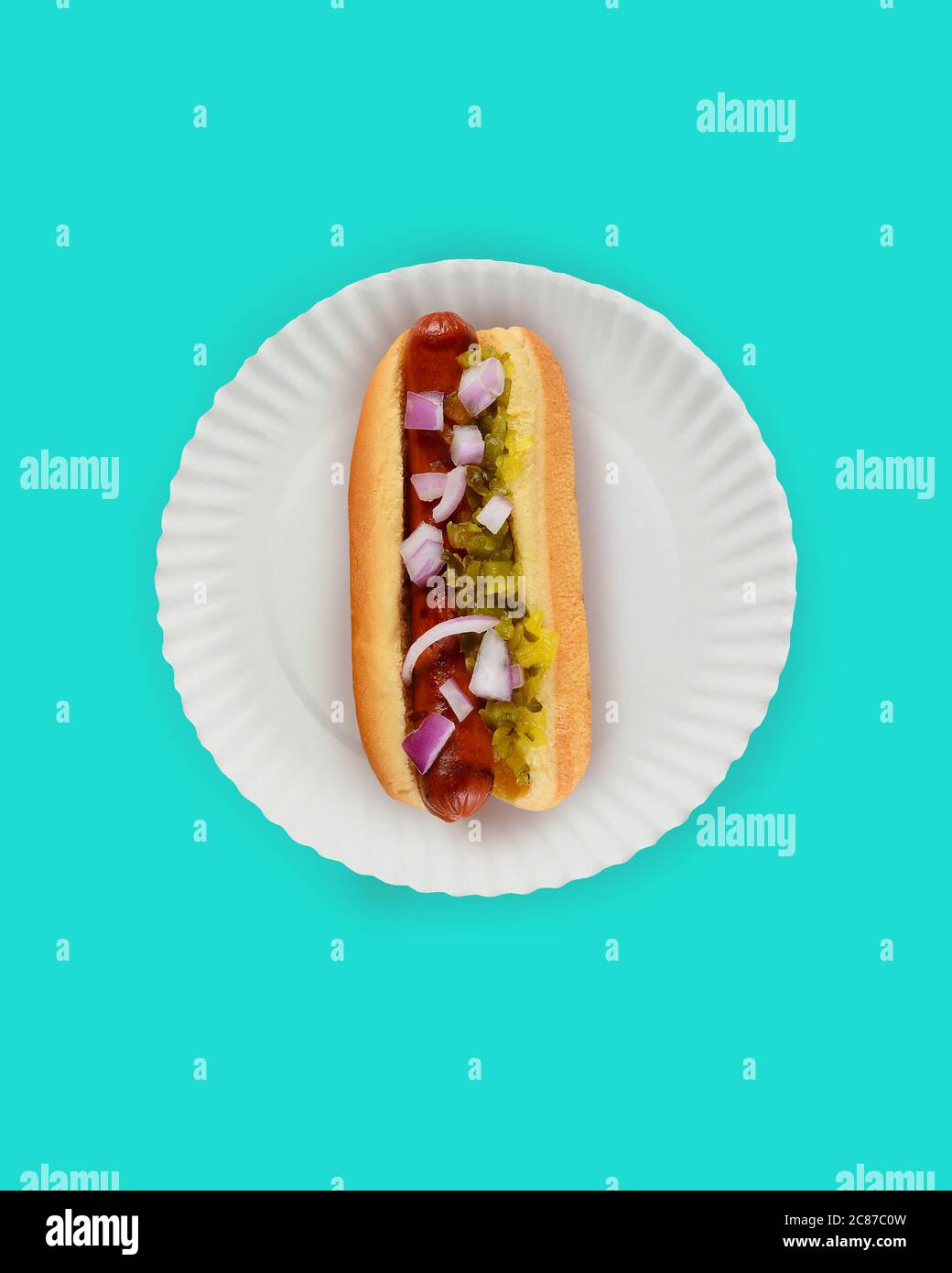 Piatto Lay Hot Dog in Bun Still Life. Falkfurter in panna con riadino e cipolle su un piatto di carta bianca su sfondo teale con spazio per la copia. Foto Stock