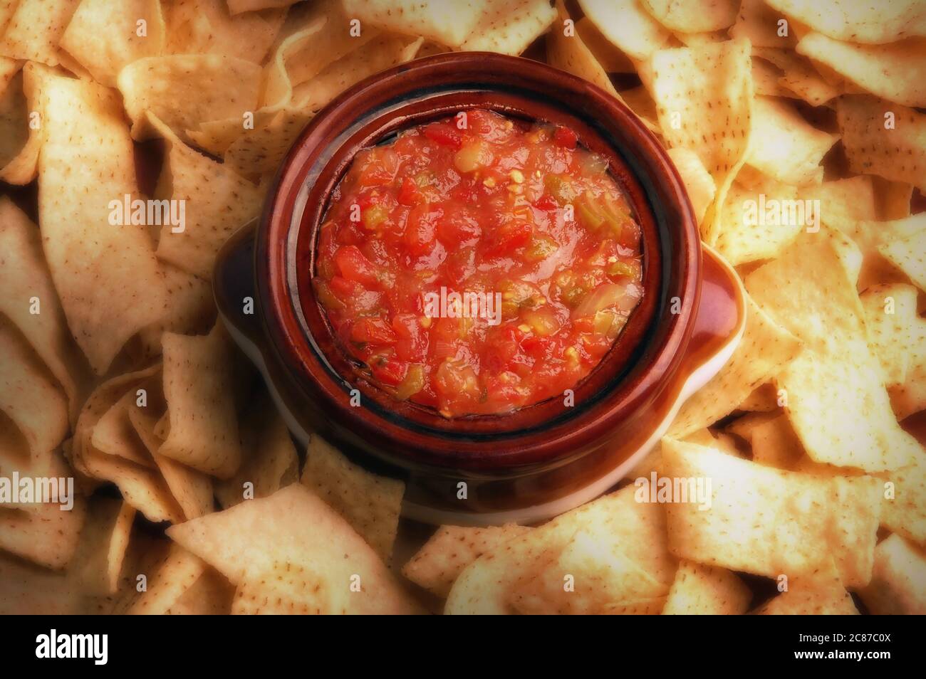 Immagine piatta di una ciotola piena di salsa circondata da scaglie di mais con luce laterale calda. Foto Stock