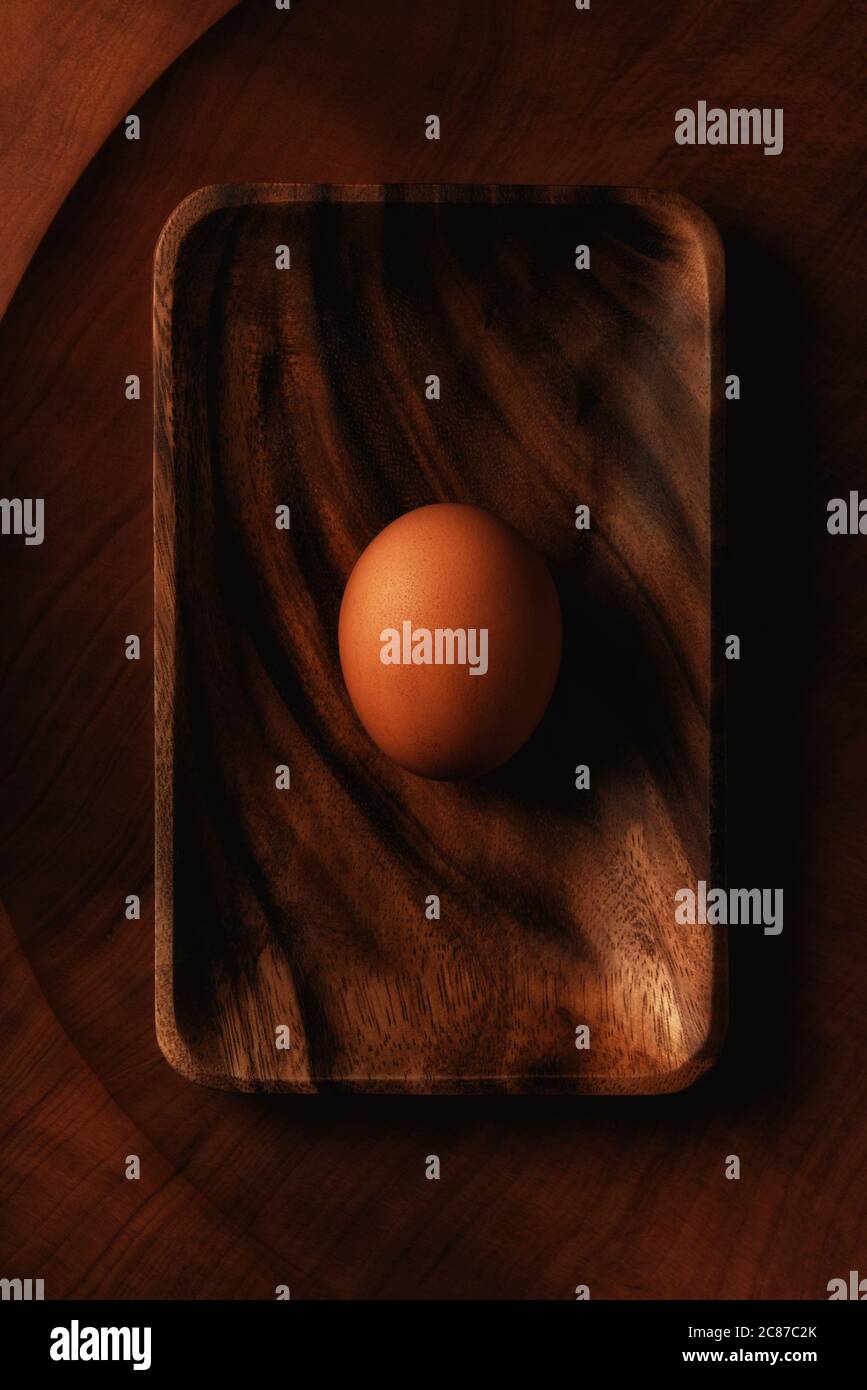 Piatto stendere la vita di un singolo uovo marrone su un vassoio di legno su un piatto rotondo di legno. Foto Stock
