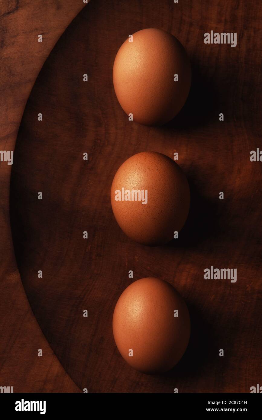 Tre uova marroni su un piatto di legno ancora vita con luce laterale calda. Foto Stock