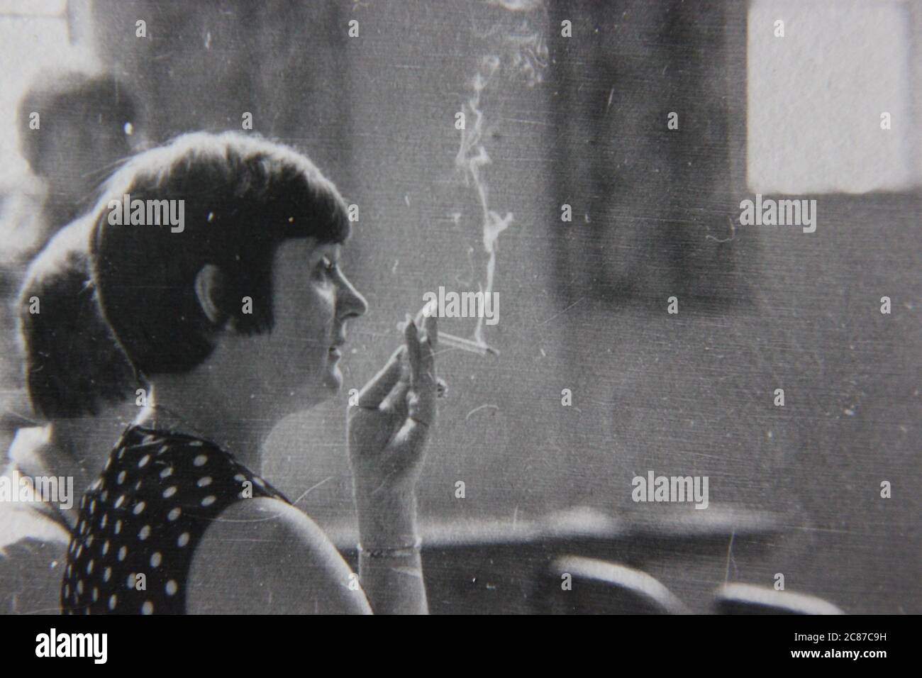 Fine anni '70 vintage nero e bianco stile di vita fotografia di una donna che fuma una sigaretta in pubblico. Foto Stock