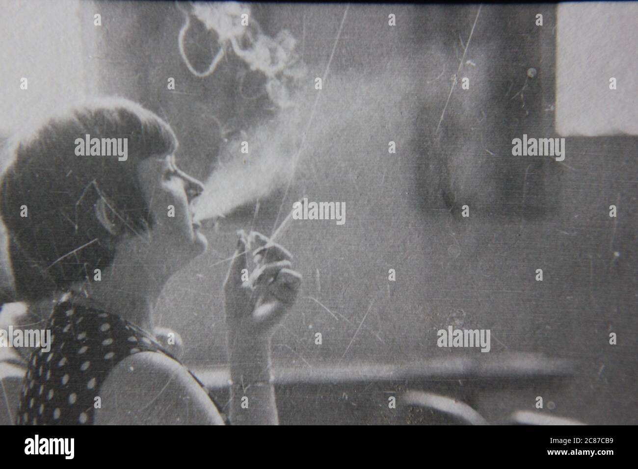 Fine anni '70 vintage nero e bianco stile di vita fotografia di una donna che fuma una sigaretta in pubblico. Foto Stock
