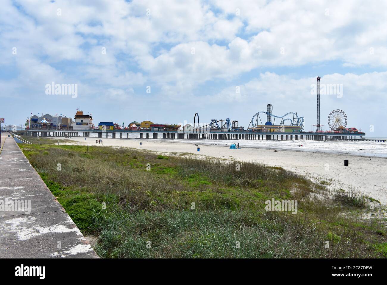 Guardando lungo la spiaggia di Galveston dal Seawall Boulevard con l'intera lunghezza del Galveston Island Historic Pleasure Pier che si estende sull'acqua. Foto Stock