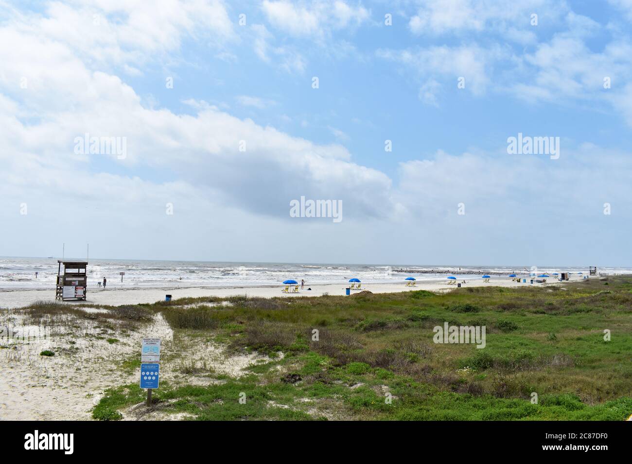 Guardando lungo Galveston Beach da Seawall Boulevard. L'erba lascia il posto alla sabbia bianca e poi al Golfo del Messico. È visibile una sedia salvagente. Foto Stock