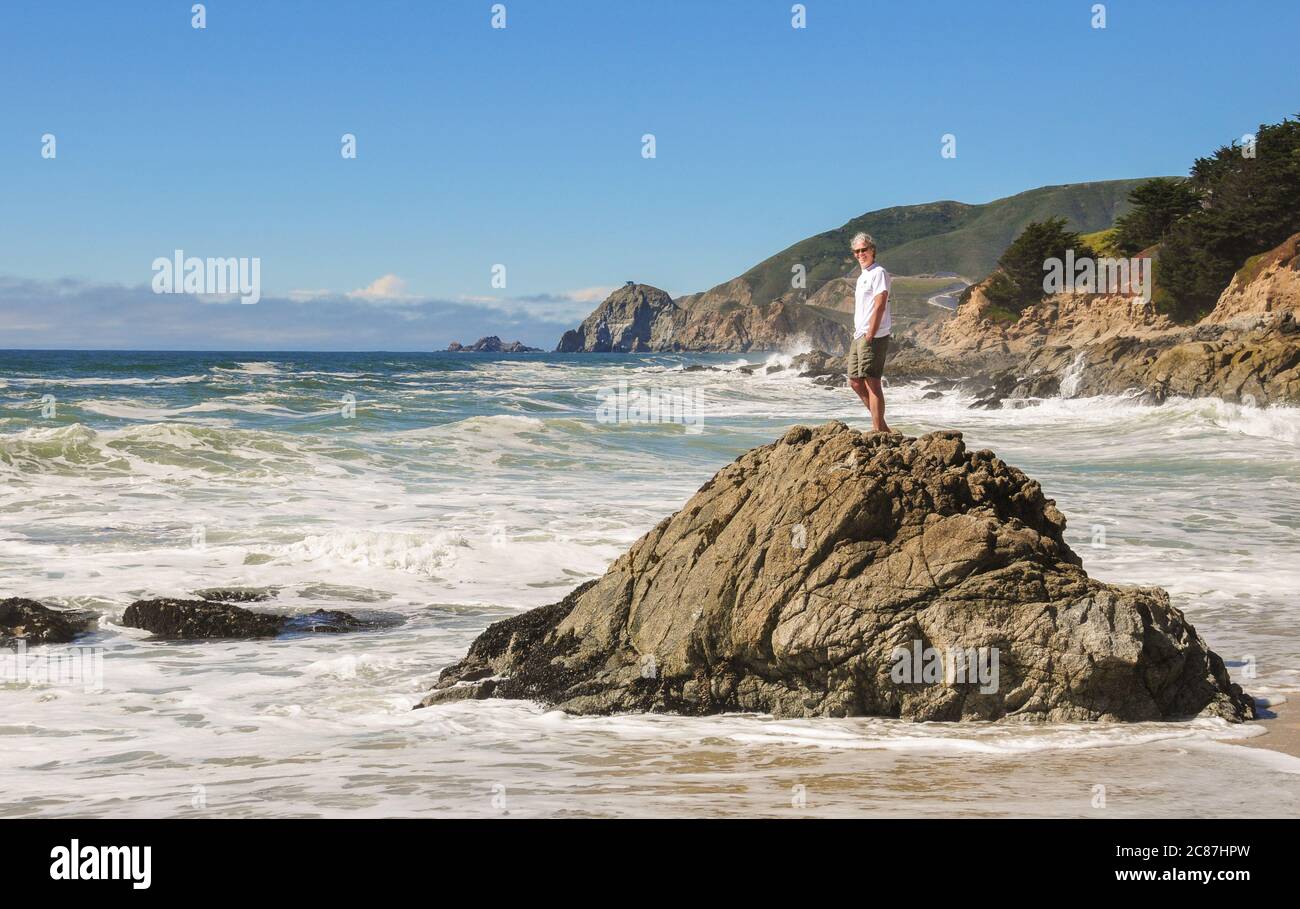 Un uomo maturo che si erge da solo su una roccia circondata dall'oceano. Versione del modello. Foto Stock