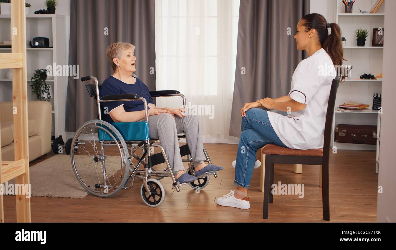Donna anziana in sedia a rotelle con disabilità che parla con l'infermiera femminile. Casa di riposo per anziani, assistenza sanitaria, assistenza sanitaria, assistenza sociale, medico e assistenza domiciliare Foto Stock
