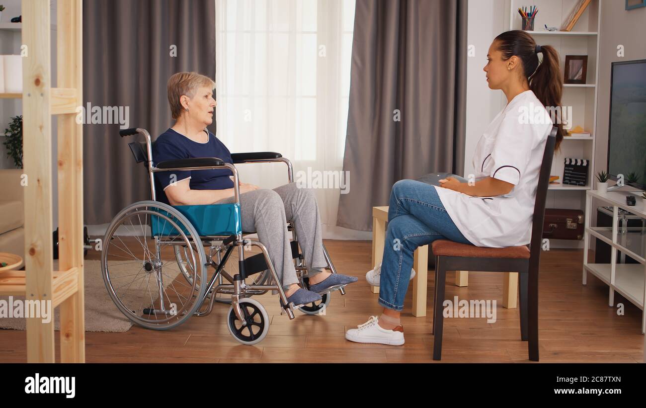 Donna anziana in sedia a rotelle con disabilità che parla con il medico. Casa di riposo per anziani, assistenza sanitaria, assistenza sanitaria, assistenza sociale, medico e assistenza domiciliare Foto Stock