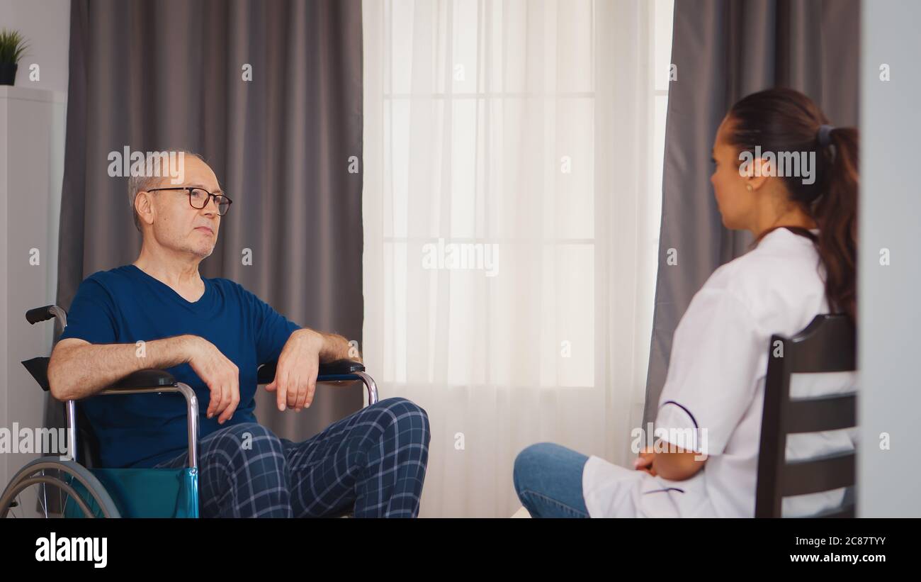 Anziano in sedia a rotelle con handicap che ha una conversazione con l'infermiere. Disabilità anziano con operatore medico in assistenza infermieristica a domicilio, assistenza sanitaria e medicina Foto Stock