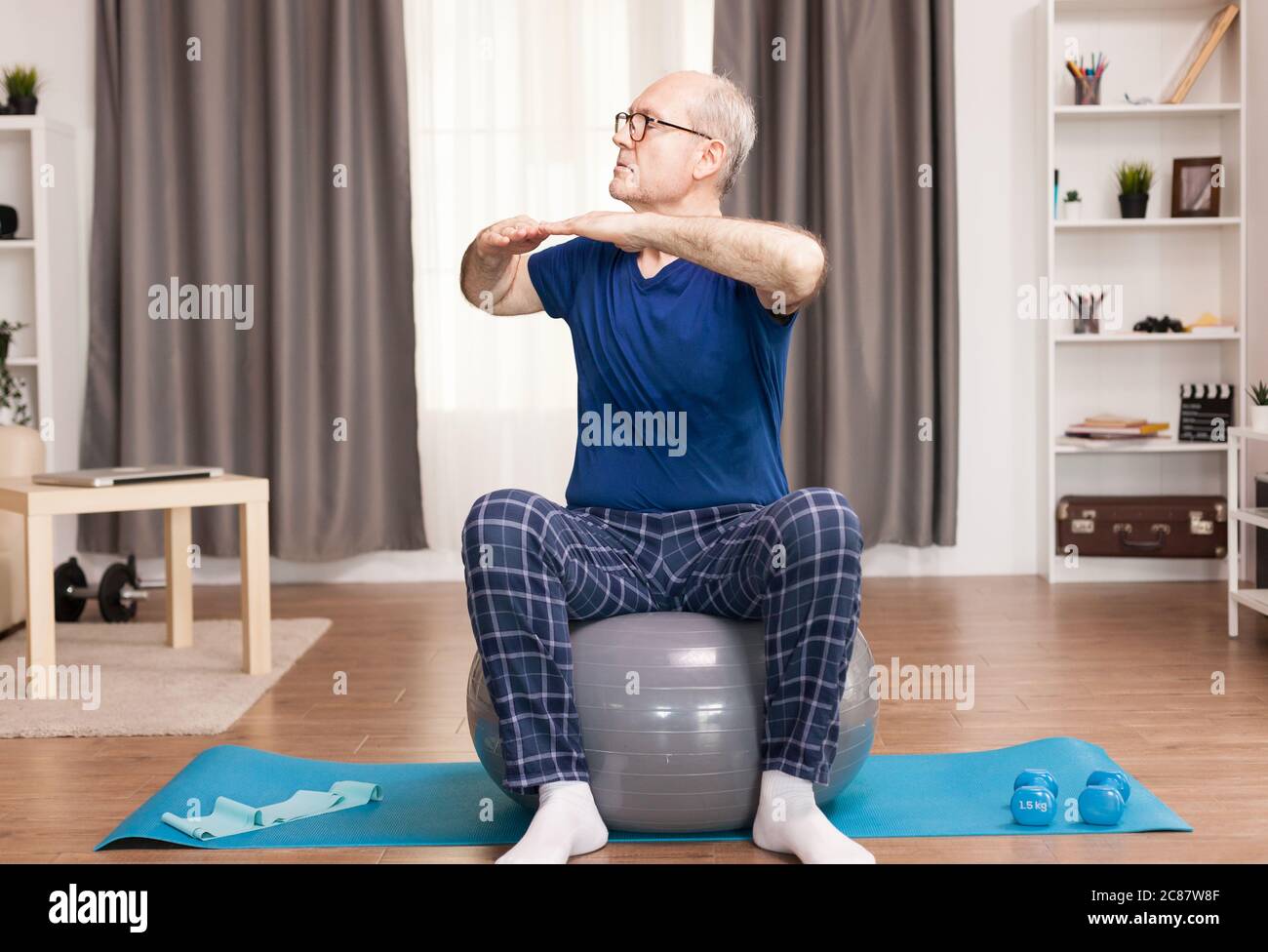 Nonno praticare sport a casa per una vita di salute. Anziano pensionato online internet esercizio di formazione a casa attività sportiva con manubri, banda di resistenza, palla svizzera all'età di anziano pensionamento. Foto Stock