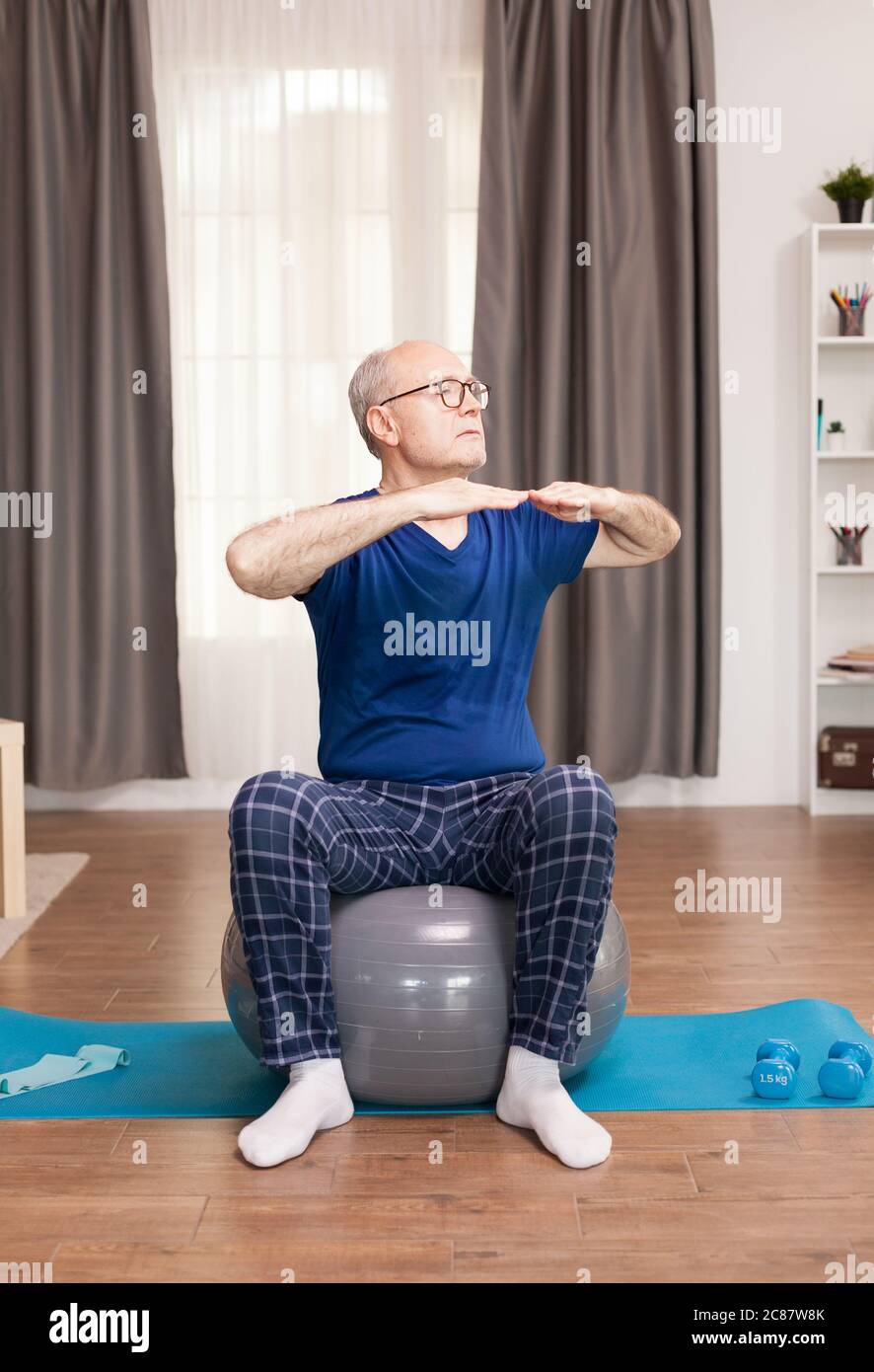 Uomo in pensione con stile di vita sano facendo esercizi di armi. Anziano pensionato online internet esercizio di formazione a casa attività sportiva con manubri, banda di resistenza, palla svizzera all'età di anziano pensionamento. Foto Stock
