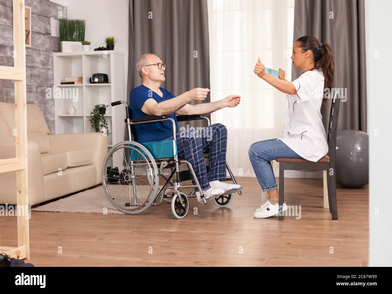 Infermiere utilizzando la banda di resistenza e spiegare al vecchio come utilizzarla. Disabili anziani disabili con lavoratore sociale in recupero terapia di supporto fisioterapia sistema sanitario di cura casa di riposo Foto Stock