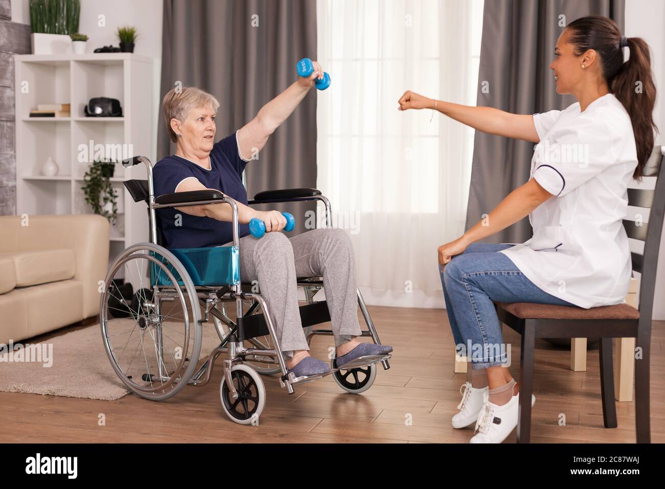 Vecchia donna non valida che addestra le braccia usando i manubri. Disabili anziani ricoverati infermiere professionista di aiuto, cura casa di riposo e riabilitazione Foto Stock