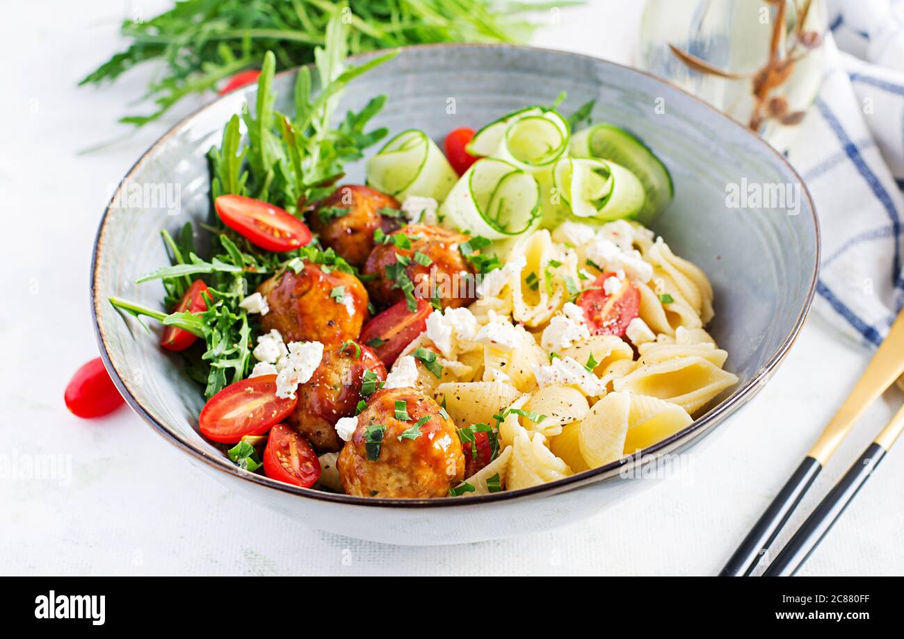 Pasta italiana. Conchiglie con polpette, formaggio feta e insalata su sfondo chiaro. Cena. Concetto di cibo lento Foto Stock