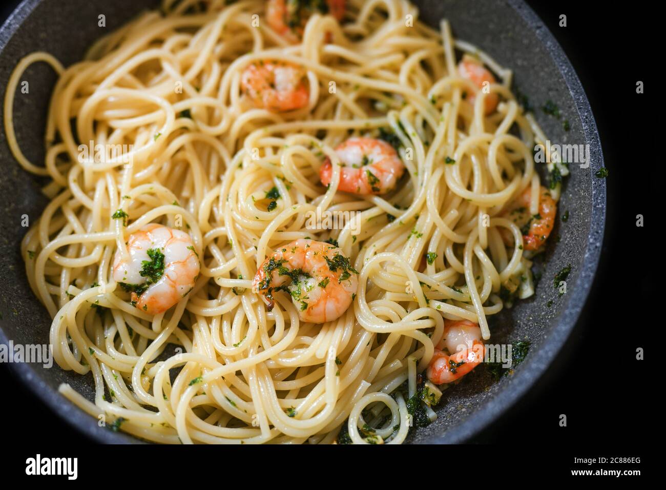 Spaghetti con prezzemolo e aglio di gamberi in una padella per un pasto di pesce mediterraneo, focalizzazione selezionata, profondità di campo ristretta Foto Stock