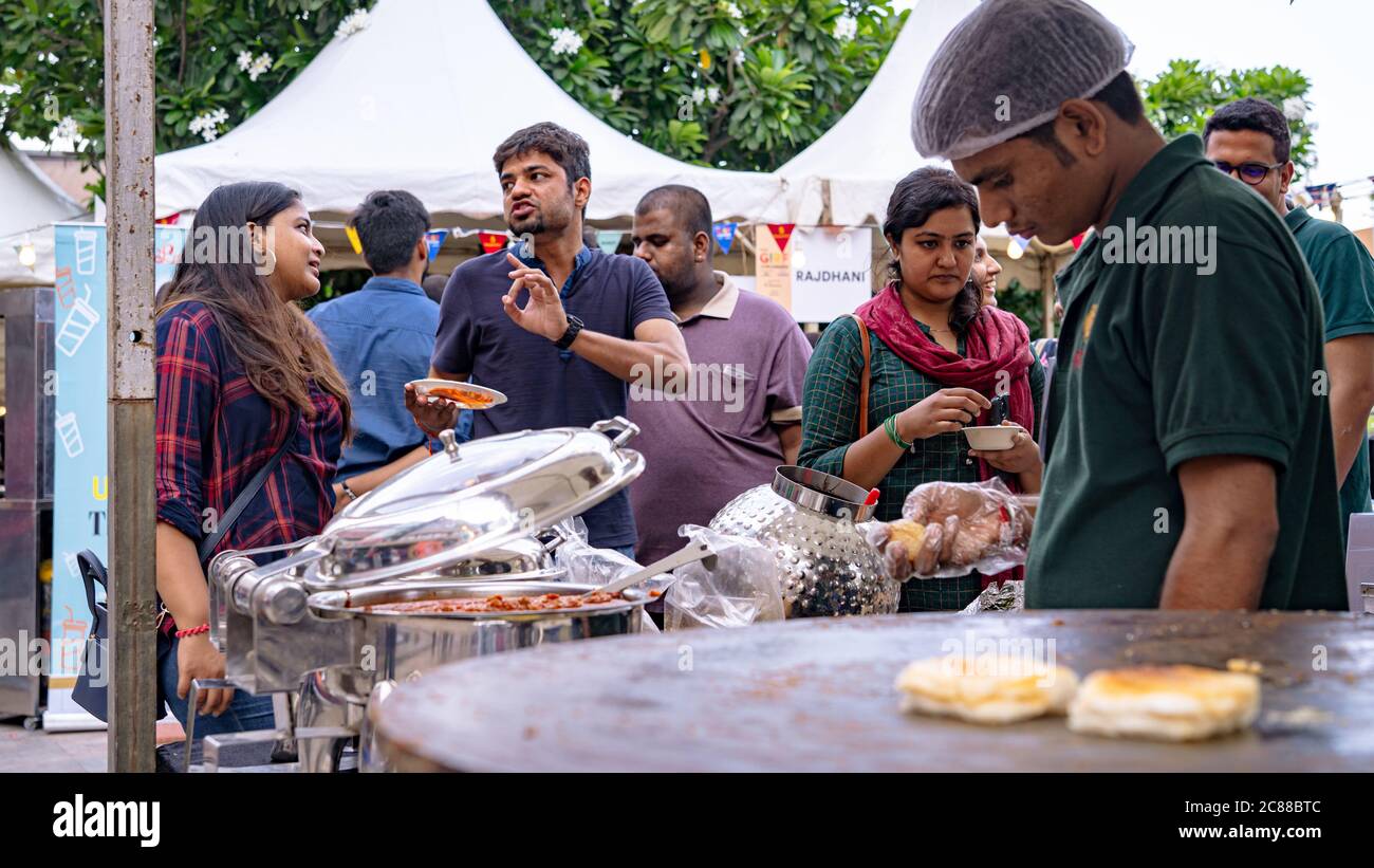 Giovani adulti che mangiano e parlano di fronte a una bancarella di cibo in un festival alimentare Foto Stock