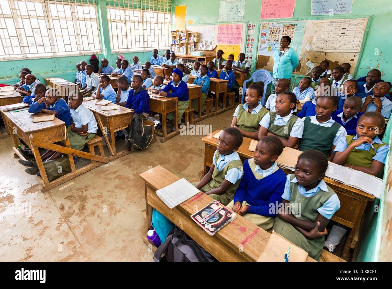 I bambini della scuola secondaria in uniforme si sedevano a banchi di legno ascoltando il loro insegnante durante la lezione, Nairobi, Kenya Foto Stock