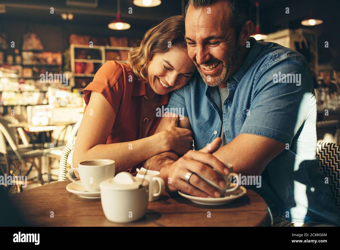 Donna sorridente e che mette la testa sulla spalla dell'uomo mentre si siede in un bar. Coppia amorevole su una data caffè insieme. Foto Stock