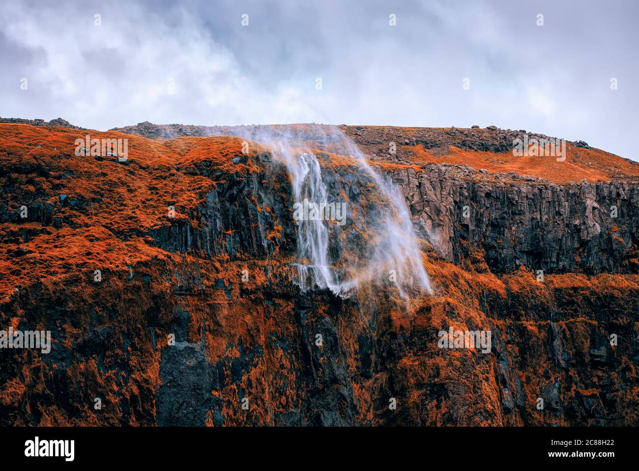 Una spettacolare cascata di acqua che viene soffiata da forti e raffiche tempeste si snoda dalla ripida scogliera situata nella vicina Seljalandsfoss a Souther Foto Stock