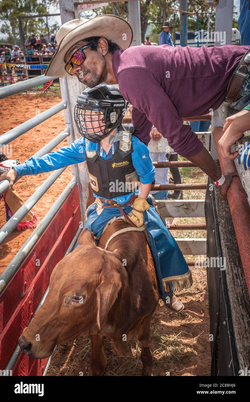 Un giovane pilota montato su un toro giovane nel rodeo shute si prepara con un po' di aiuto da un altro cowboy al Mt Garnet, Queensland. Foto Stock