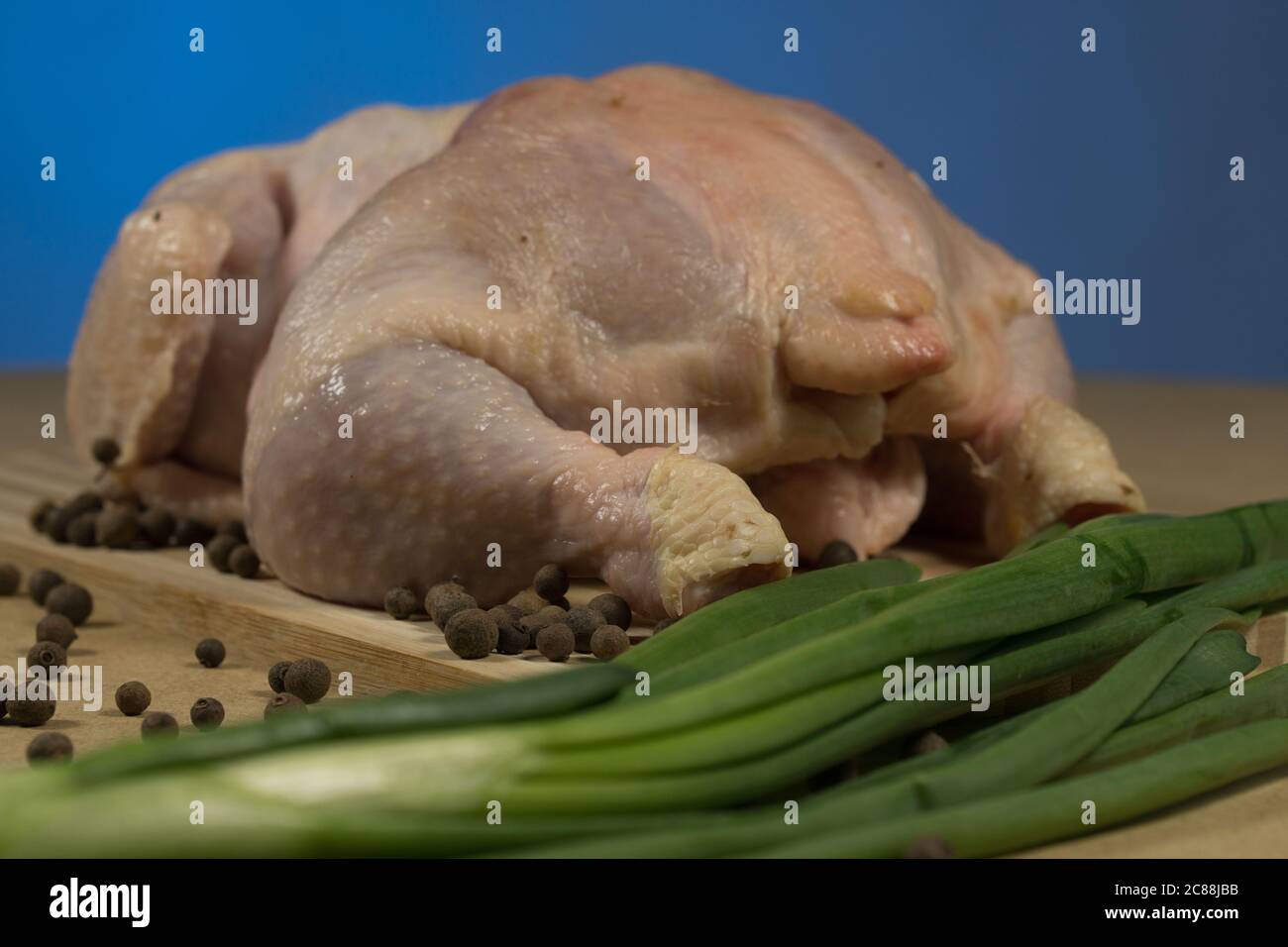 Carcassa di pollo cruda con spezie ed erbe su un tagliere su un tavolo di legno Foto Stock