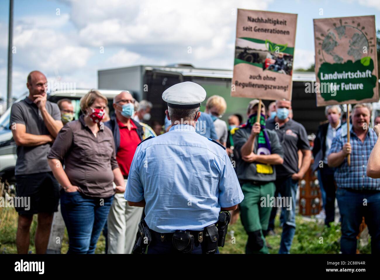 22 luglio 2020, Renania Settentrionale-Vestfalia, Rheda-Wiedenbrück: Un poliziotto assicura la contromondimostrazione degli agricoltori. Gli attivisti per i diritti degli animali dell'Ufficio tedesco per il benessere degli animali si presentano davanti alla fabbrica di carne di Tönnies con striscioni e cartelli. Il loro motto è: 'Tönnies uccide! La gente soffre, gli animali muoiono'. Dalla scorsa settimana il macello è stato nuovamente aperto. Attualmente, vi vengono uccisi fino a 10,000 maiali ogni giorno. Foto: David Inderlied/dpa Foto Stock