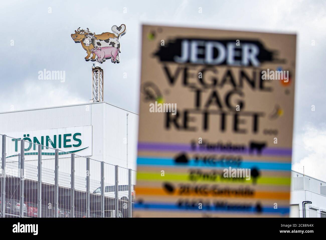 22 luglio 2020, Renania settentrionale-Vestfalia, Rheda-Wiedenbrück: Un manifesto di attivisti per i diritti degli animali dice: 'Ogni giorno vegano salva...' Gli attivisti per i diritti degli animali dell'Ufficio tedesco per il benessere degli animali si presentano davanti alla fabbrica di carne di Tönnies con striscioni e cartelli. Il loro motto è: 'Tönnies uccide! La gente soffre, gli animali muoiono'. Gli agricoltori della regione hanno organizzato una contromondimostrazione. Dalla scorsa settimana il macello è stato riaperto. Attualmente, vi vengono uccisi fino a 10,000 maiali ogni giorno. Foto: David Inderlied/dpa Foto Stock