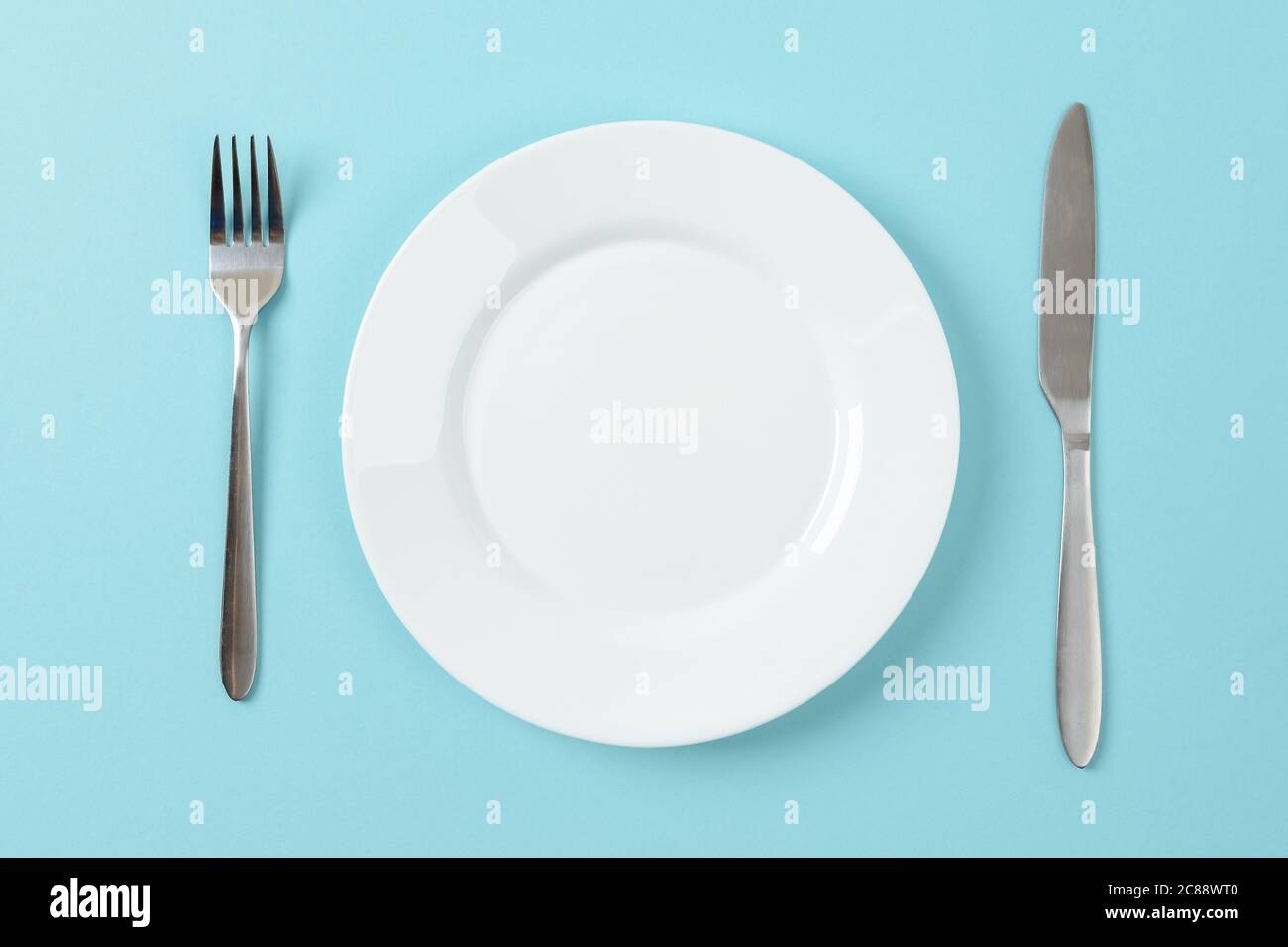 Piatto da pranzo bianco vuoto, coltello da tavola e forchetta su sfondo blu. Impostare la tabella. Spazio di copia su piatto per la progettazione di alimenti. Vista dall'alto. Foto Stock