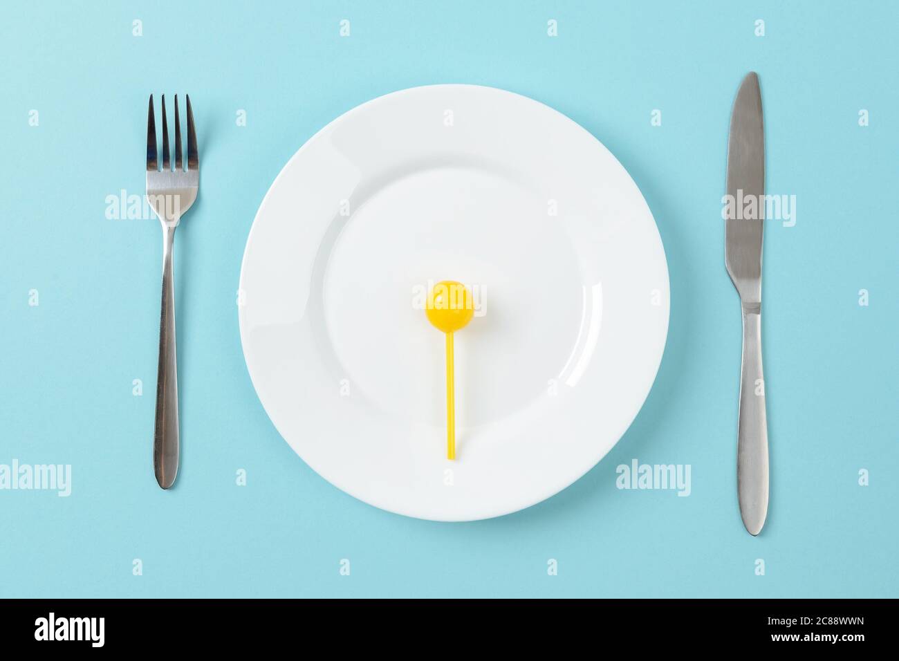 Caramello giallo dolce caramello caramello su un piatto da pranzo bianco, coltello da tavola e forchetta su sfondo blu. Concetto di alimentazione malsana con carboidrati in eccesso. Foto Stock