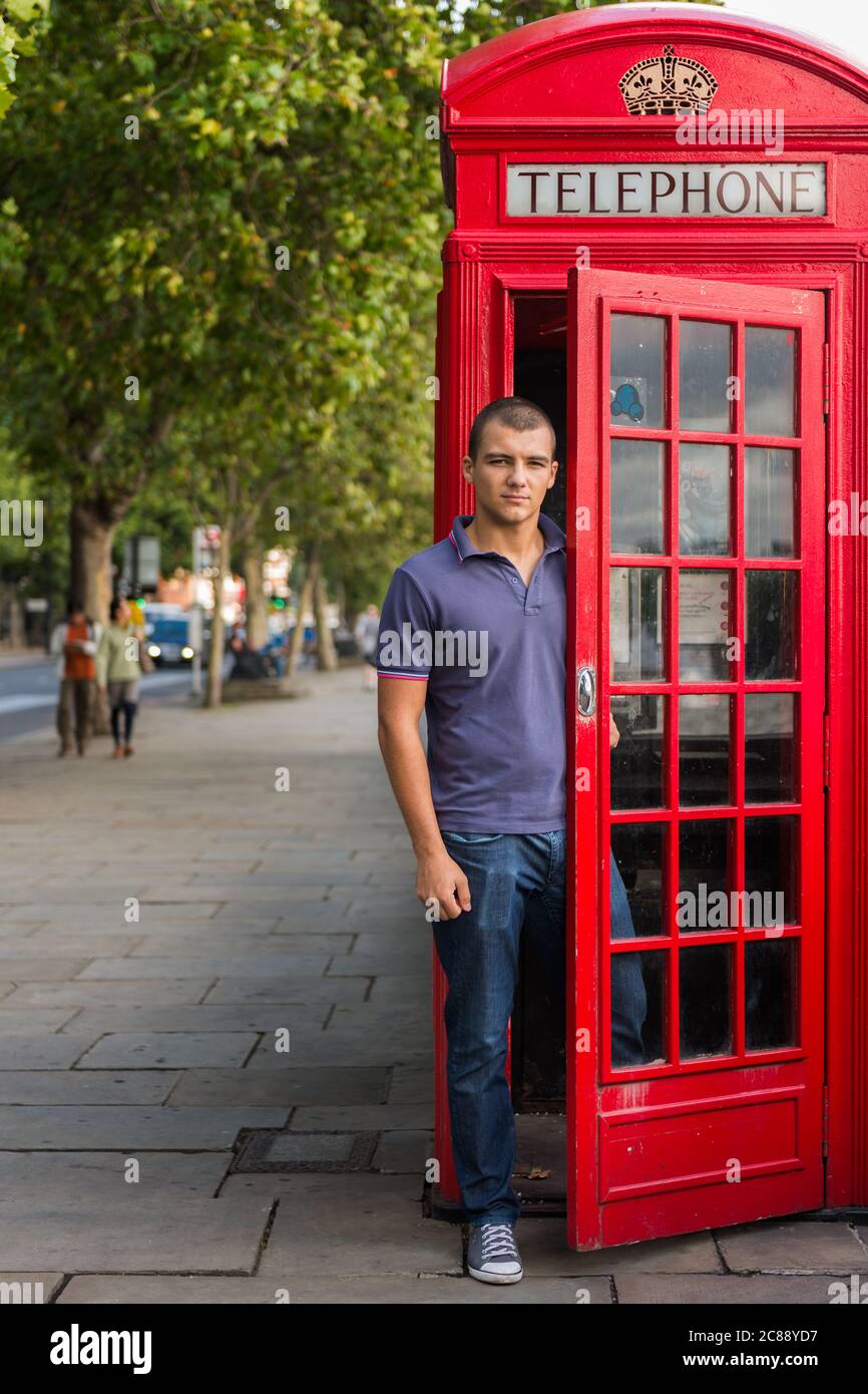 Giovane uomo turista maschile in posa per foto da tradizionale telefono rosso box al Embankment a Londra Regno Unito nel 2013 Foto Stock