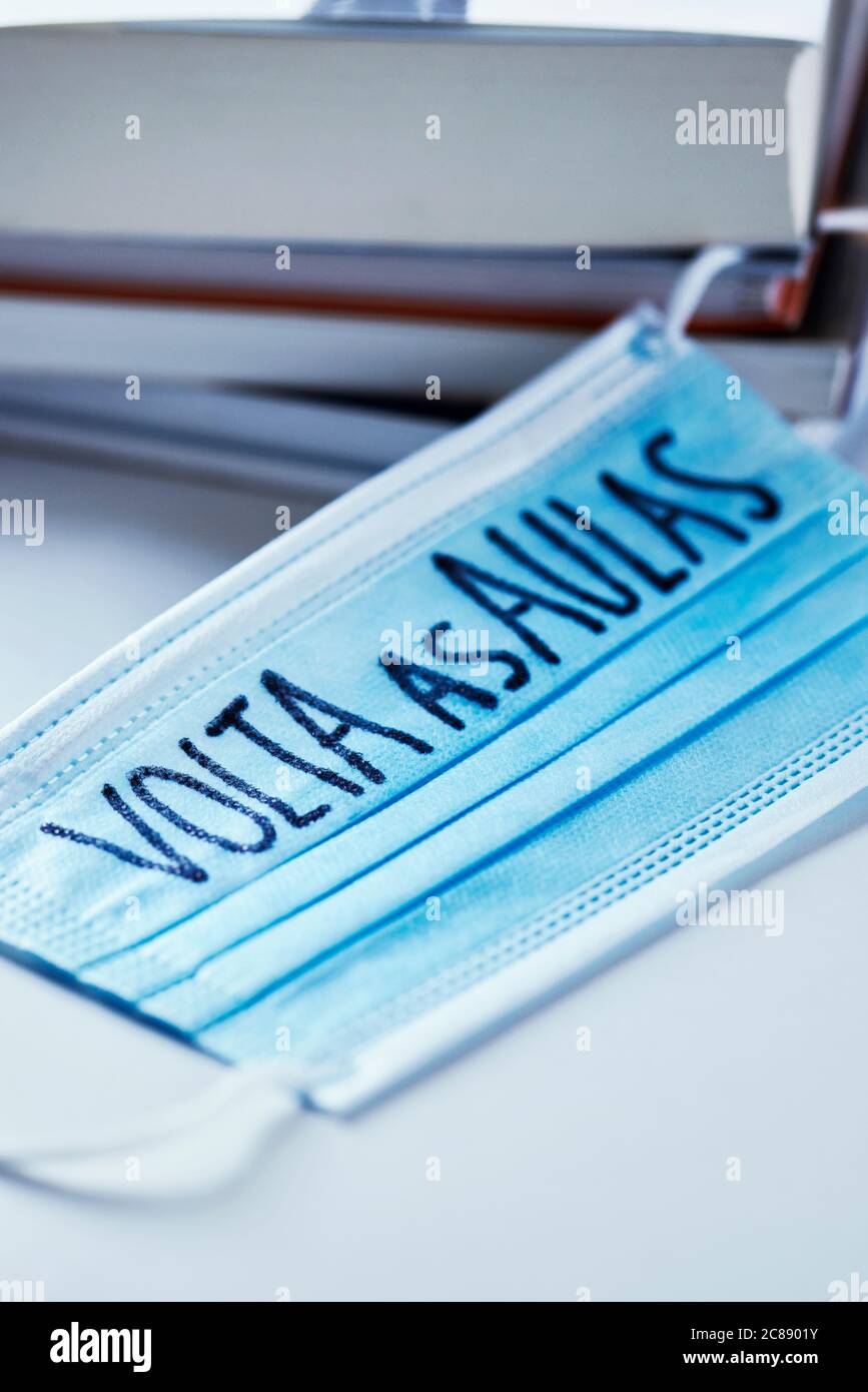 closeup di un mucchio di libri e una maschera chirurgica blu con il testo di ritorno a scuola scritto in portoghese, che raffigura la necessità di prevenire l'infezione a. Foto Stock