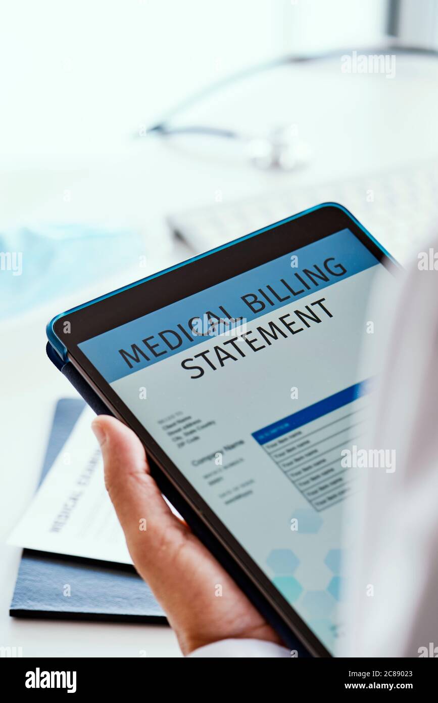 primo piano di un medico caucasico, alla sua scrivania d'ufficio, che controlla una dichiarazione di fatturazione medica in un tablet digitale Foto Stock