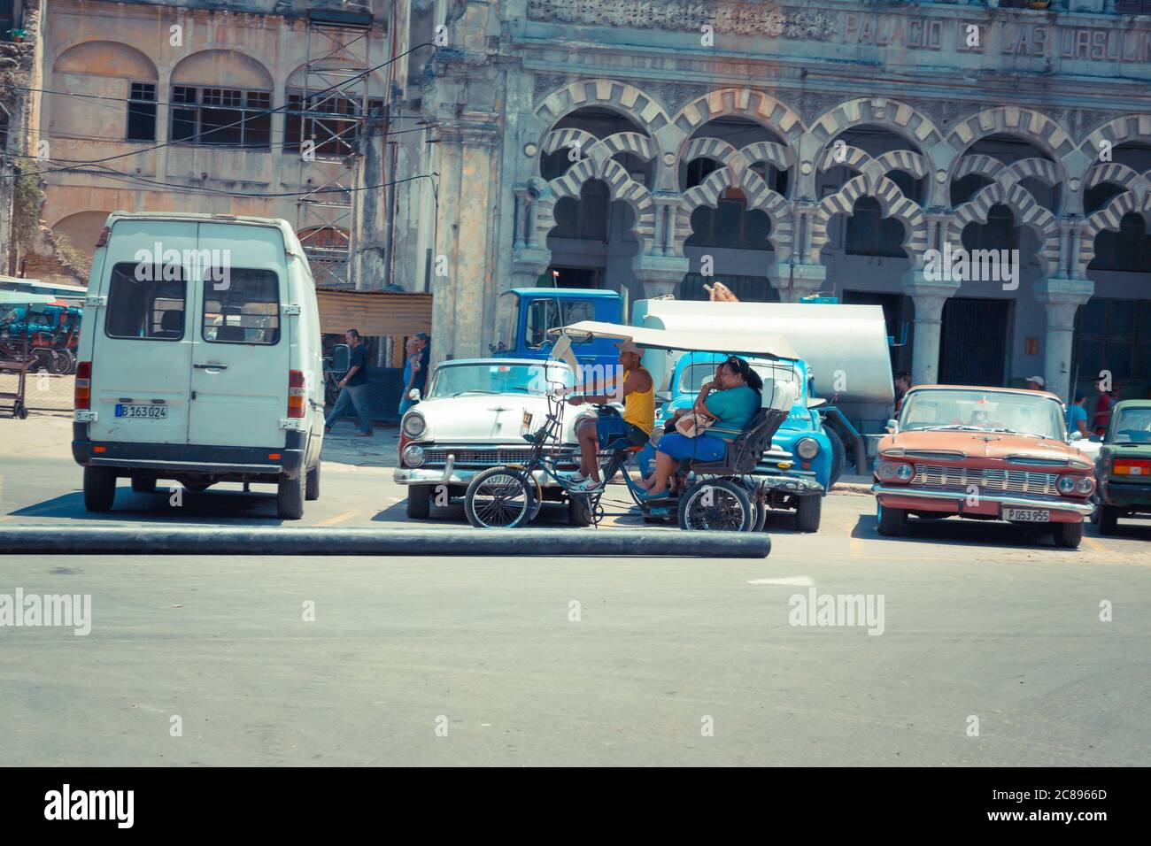 Havana / Cuba - 04.15.2015: Un tipico taxi cubano in bicicletta, aka bicitaxi in bicicletta per le strade di l'Avana passando davanti alle classiche auto americane, Isola o Foto Stock