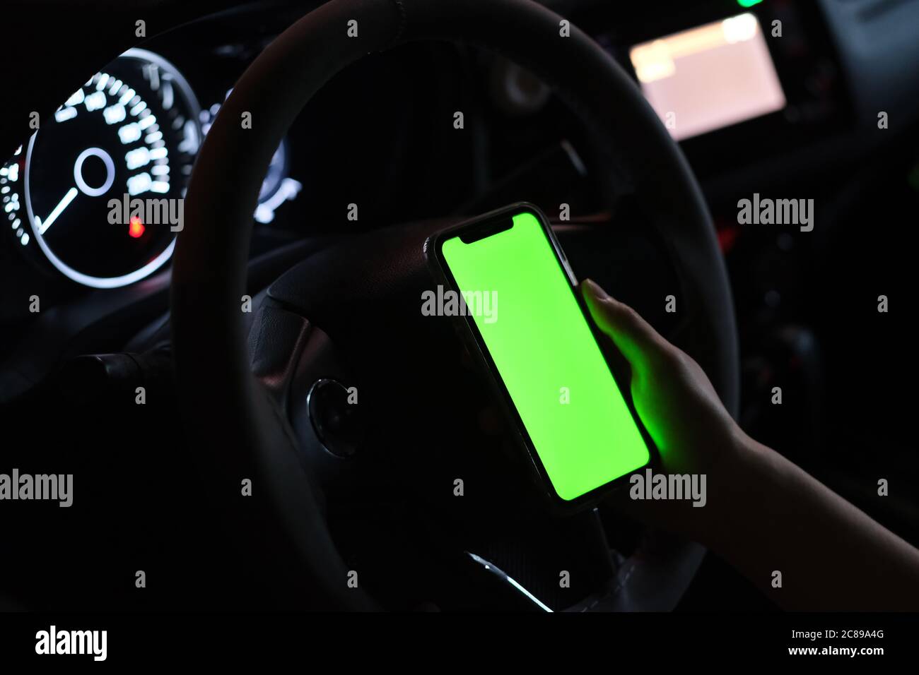 primo piano con una mano che tiene in mano lo smartphone con schermo verde in auto di notte. sfocatura dello sfondo Foto Stock