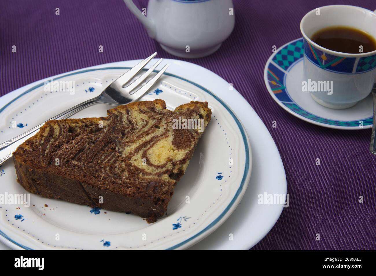 Primo piano di un piatto con una fetta di torta di cioccolato e vaniglia nota come torta di tigre o zebra, accanto a una tazza di caffè Foto Stock