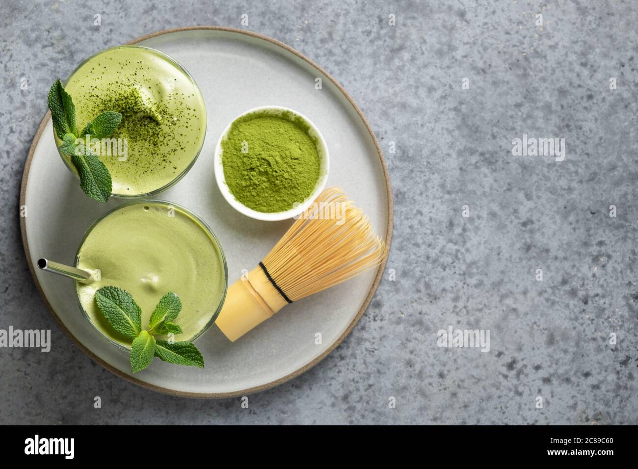 Due bicchieri di tè Dalgona matcha latte, bambu' e matcha polvere su grigio. Foto Stock