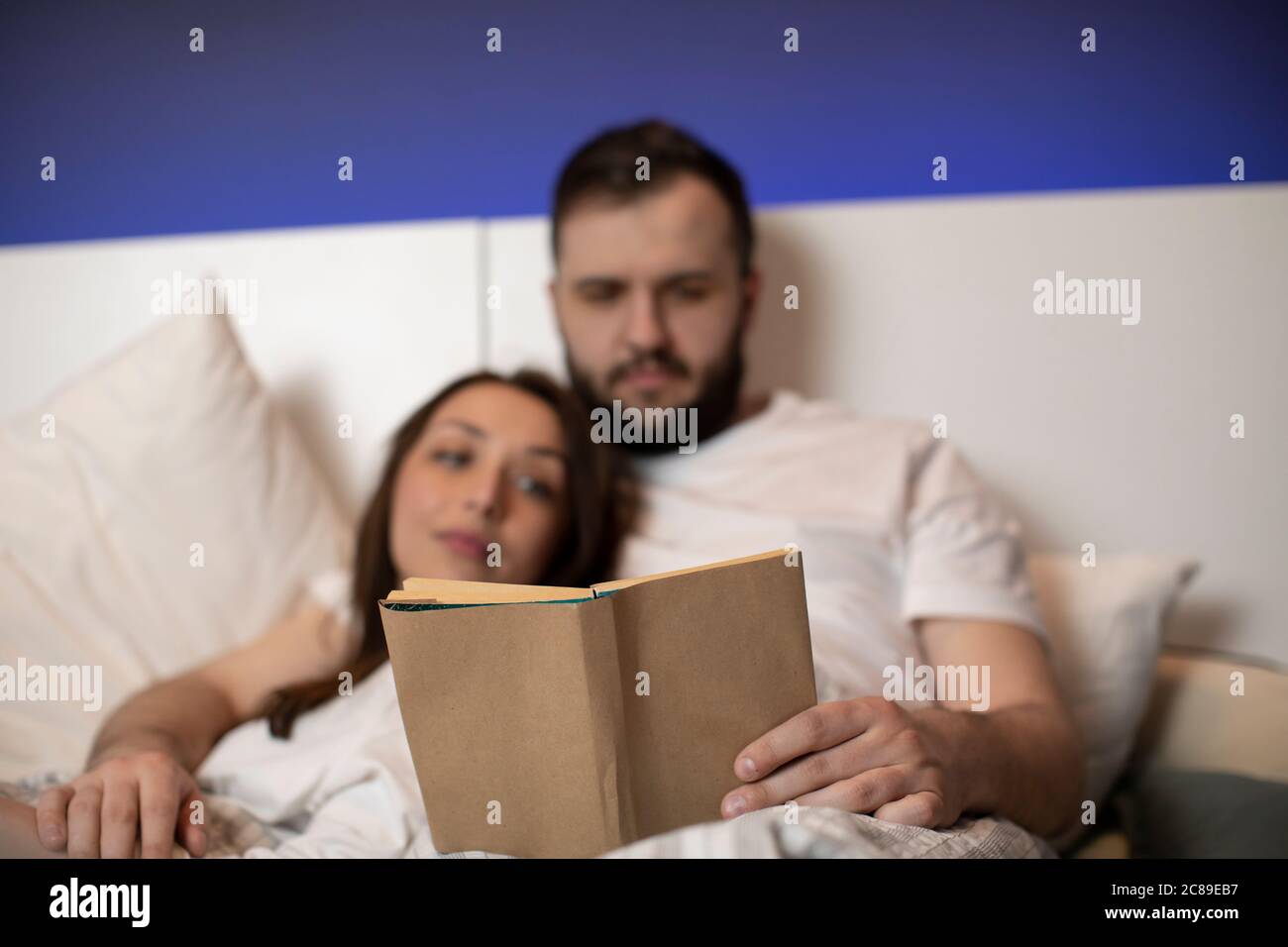 coppia di amanti che indossano pigiami bianchi che leggono un libro per due  a letto insieme Foto stock - Alamy