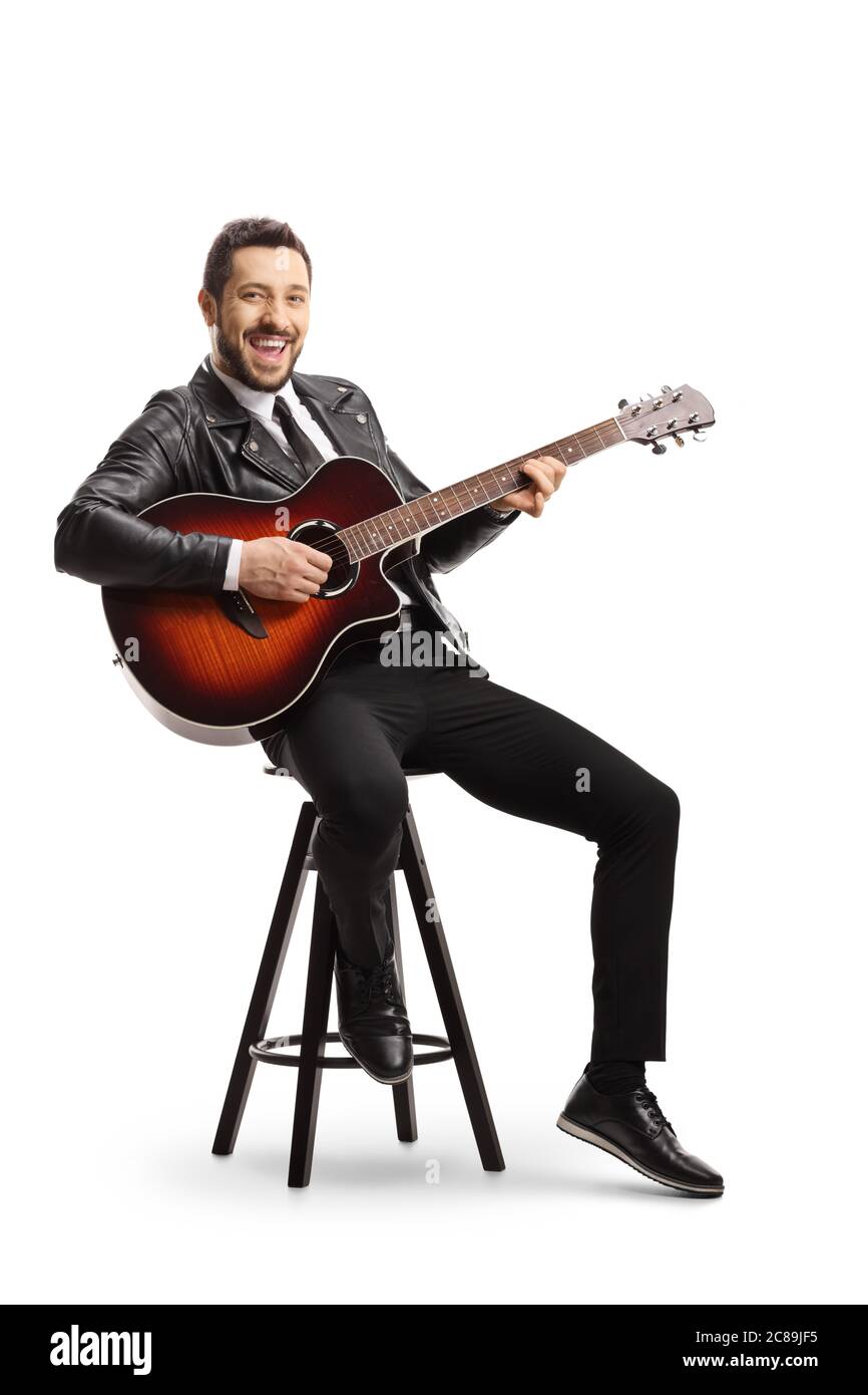 Allegro musicista ragazzo che suona una chitarra acustica e seduto su una sedia isolata su sfondo bianco Foto Stock