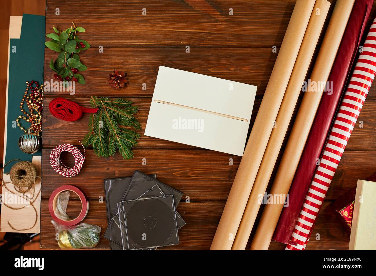 Vista ad alto angolo della scatola regalo bianca non avvolta sul tavolo di legno scuro con carta da imballaggio, rotoli di spago che decorano elementi giorni festivi e regali conc Foto Stock