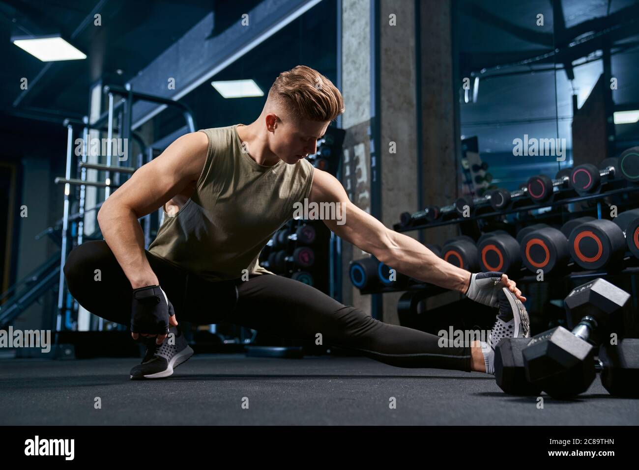 Allestitore caucasico muscolare in abbigliamento sportivo che si estende sul pavimento in club sportivo. Vista frontale della bella tomaia sportiva in palestra vuota. Concetto di bodybuilding, stile di vita sano. Foto Stock