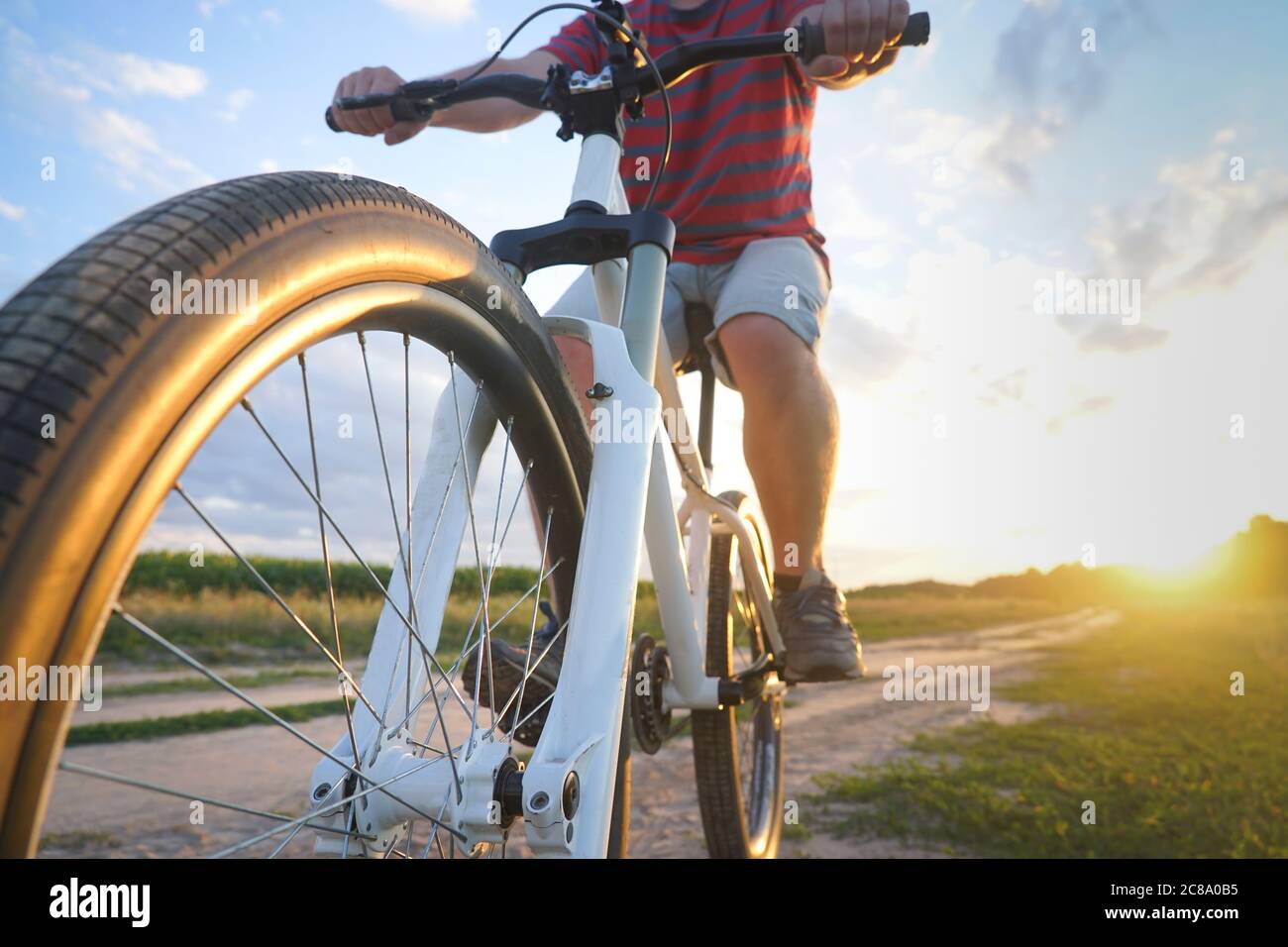 Un ragazzo su una mountain bike in una T-shirt rossa e con uno zaino corre su una strada sterrata al tramonto Foto Stock