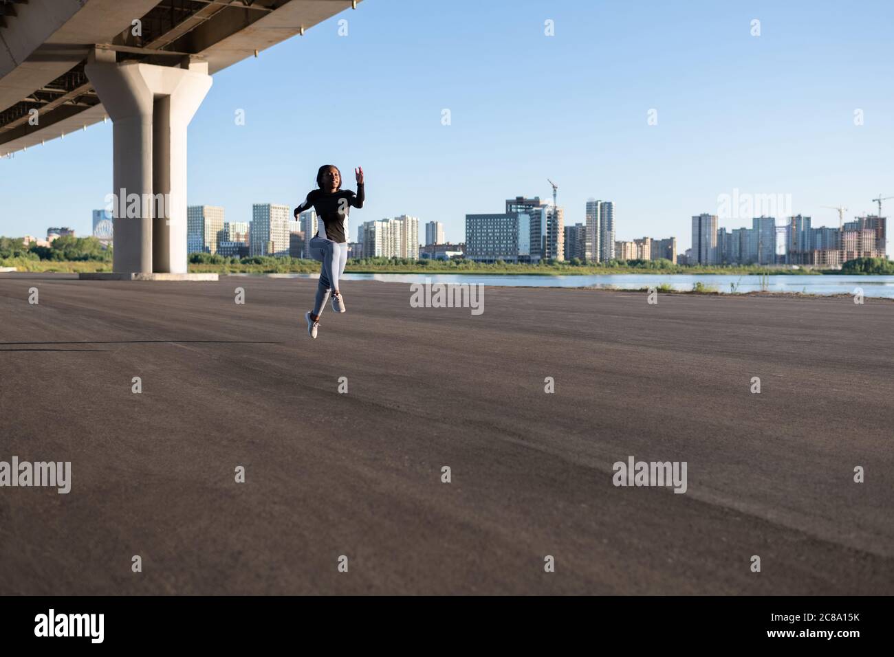Forte atleta etnico che salgono in corsa durante l'allenamento sotto ponte di mattina Foto Stock