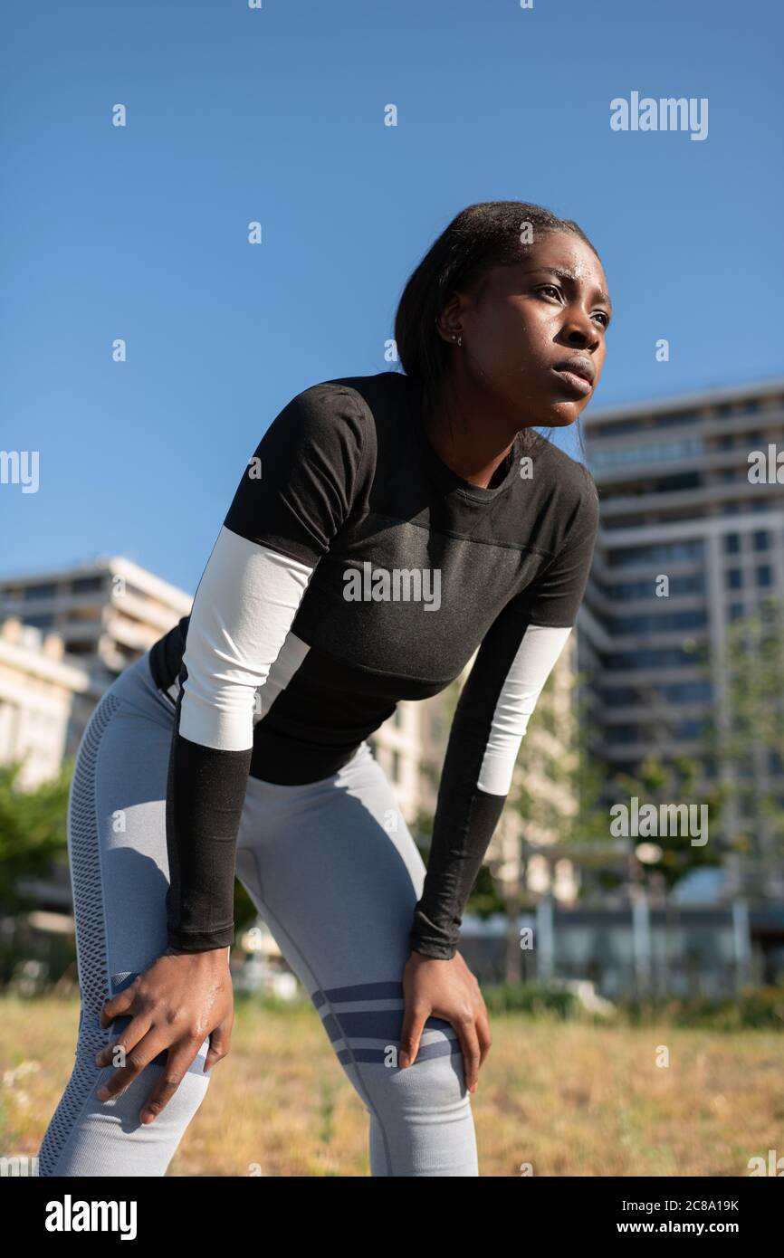 L'angolo basso dell'atleta nero esausto si inclina in avanti e guarda via durante la pausa Foto Stock