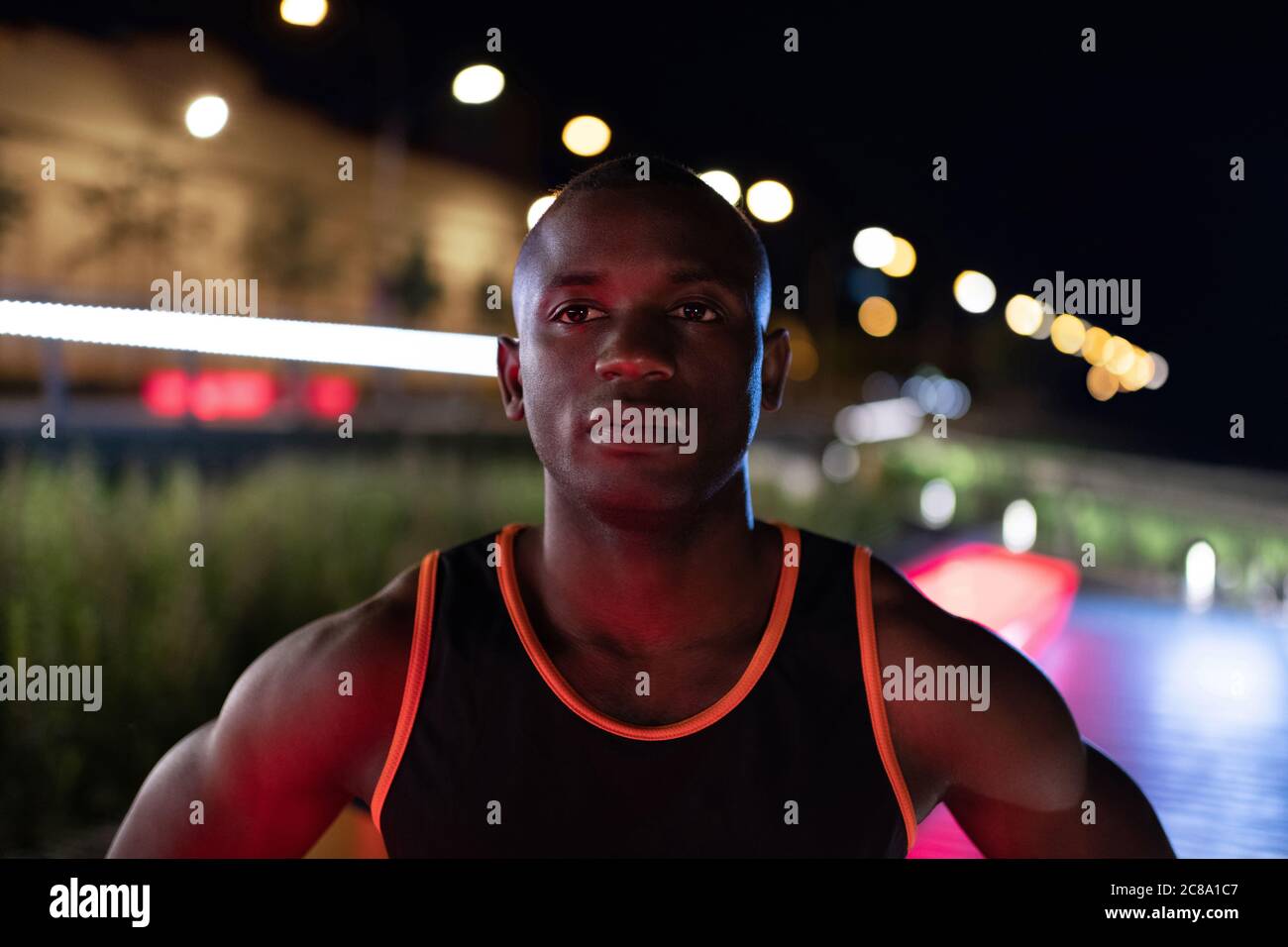 Runner nero sicuro che guarda via durante l'allenamento sulla strada della città di notte Foto Stock