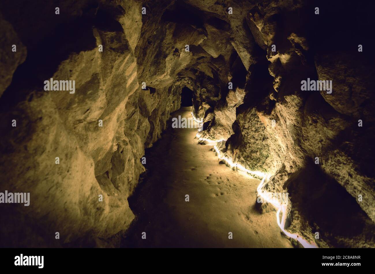 percorso sotterraneo diritto in una grotta di pietra illuminata da luce gialla con parete di roccia e un buco nero alla fine Foto Stock