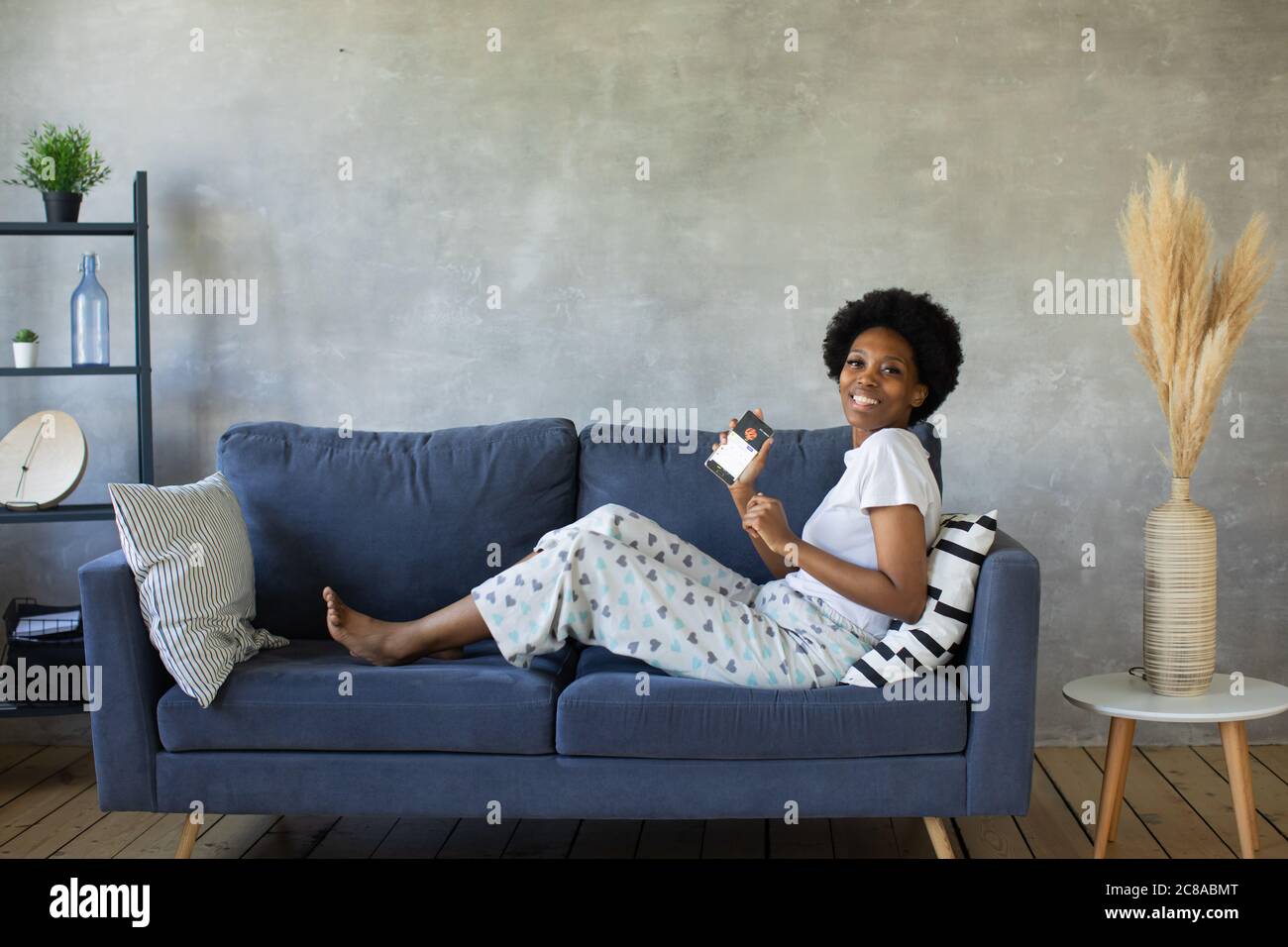 Ragazza afroamericana che balla con il suo telefono sul divano in una stanza accogliente Foto Stock