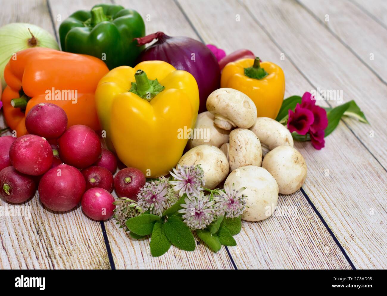 Verdure e fiori freschi raccolti organici esposti su tavola di legno in disposizione artistica per incoraggiare pasti sani Foto Stock