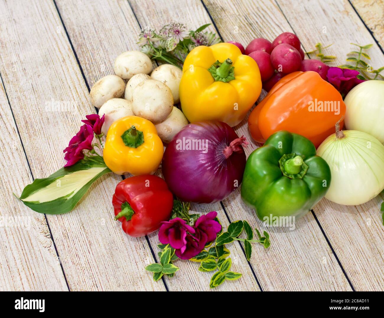 Verdure e fiori freschi raccolti organici esposti su tavola di legno in disposizione artistica per incoraggiare pasti sani Foto Stock