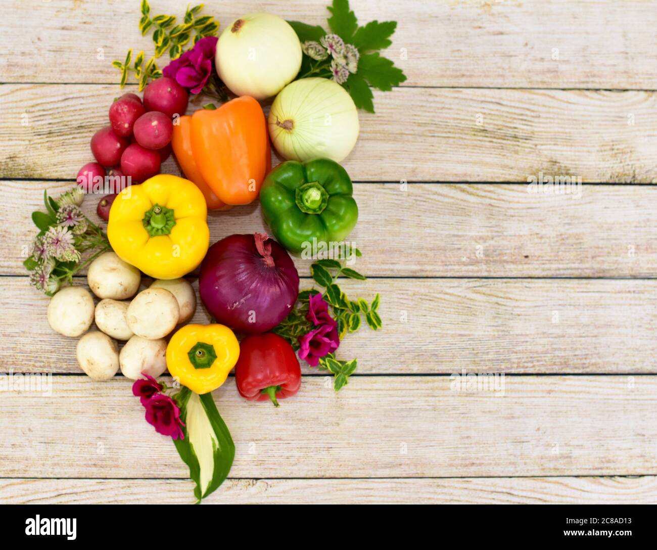 Verdure e fiori freschi raccolti organici esposti su tavola di legno in disposizione artistica per incoraggiare pasti sani Foto Stock