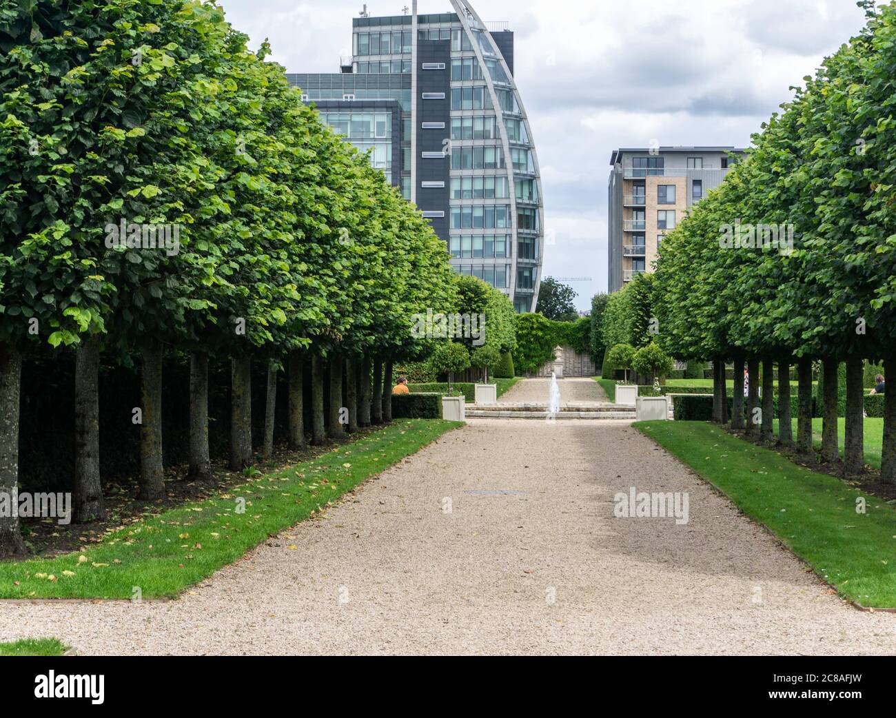 Un viale alberato nei giardini del Royal Hospital Kilmainham che conduce a una fontana con gli edifici del quartiere Hueston sullo sfondo. Foto Stock
